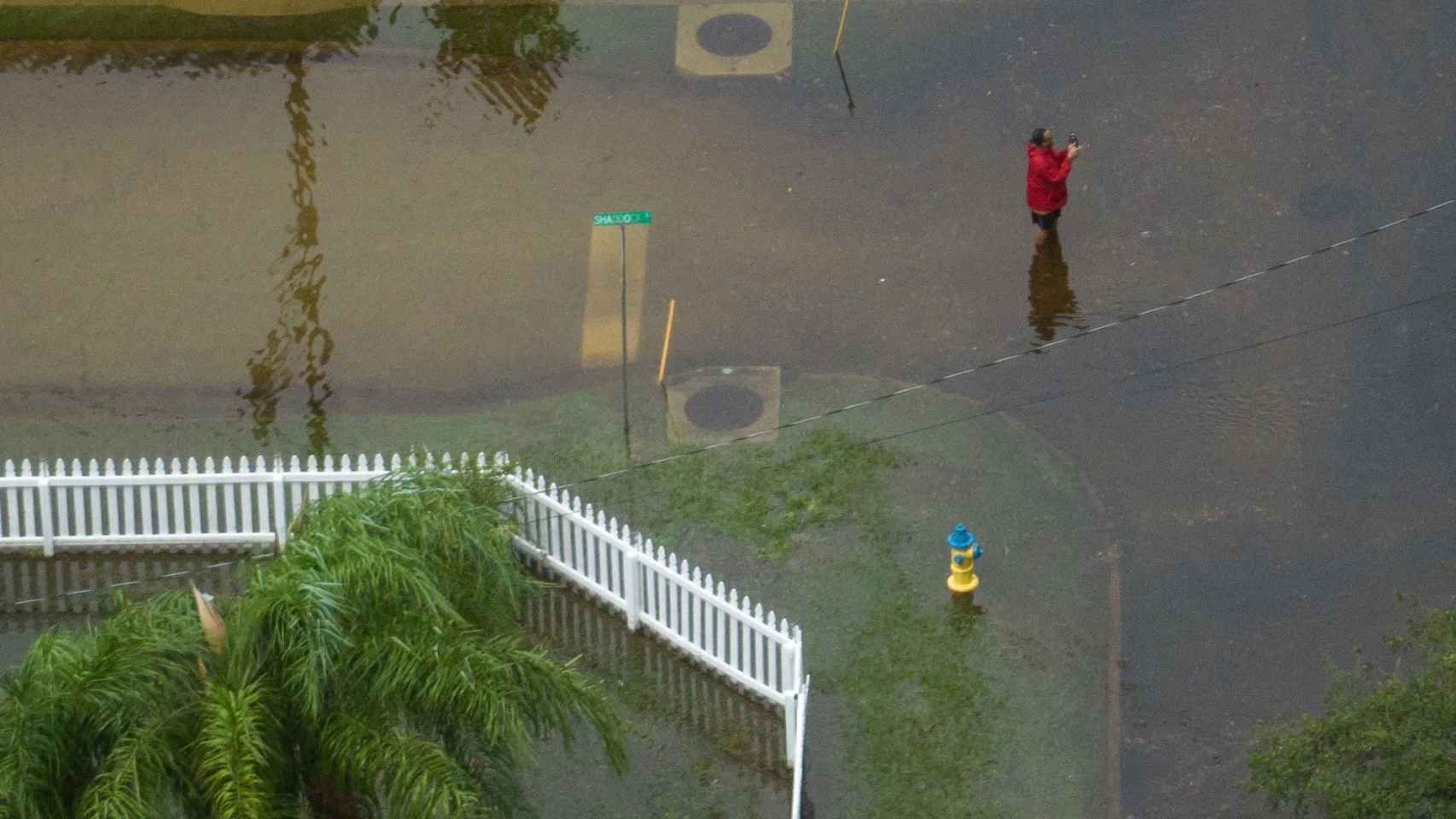 Uma mulher a tirar fotografias no meio de uma rua inundada em Tarpon Springs.